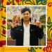 Young man in a black jacket holds up two illustrated brochures in front of a colorful mural background.