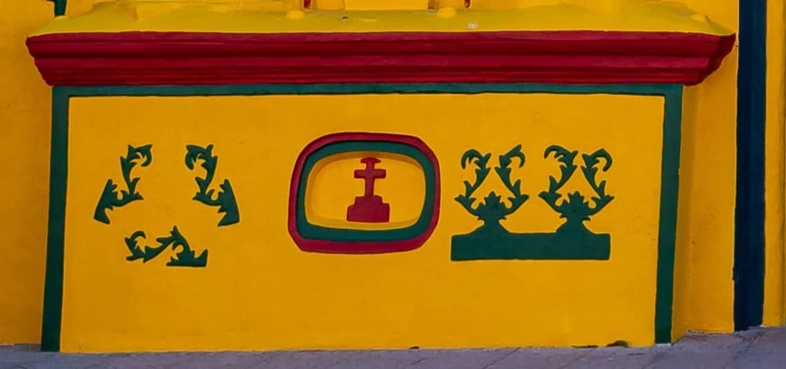 Al lado izquierdo está la Cruz que representa el sacrificio de Jesús. Ramilletes de corozo y tres ramas de palma: Padre, Hijo y Espiritu Santo, la Santísima Trinidad cristiana.