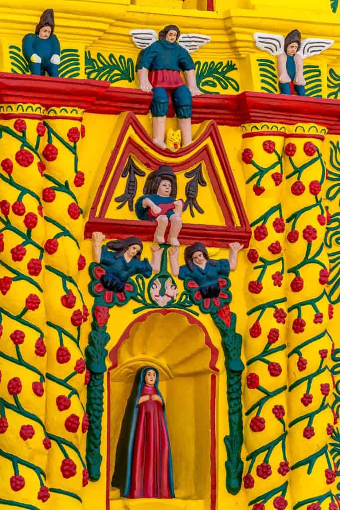 La Virgen de Concepción está en la hornacina. A los lados están, según ciertas interpretaciones, dos sirenas. Sin embargo para los habitantes son dos ángeles con zancos (en realidad en toda la fachada hay 13 ángeles con zancos) que representan la danza tradicional del Chitik. Las columnas están decoradas con enredaderas de mora, que representa un alimento sagrado. Con una guitarra está Hun Batz, personaje del Popol Vuh que representa a los artistas y los músicos. Sentado con las alas abiertas está Hunahpú, uno de los gemelos del Popol Vuh. Los ángeles con zancos protegen al sagrado maiz.