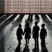 Four children stand in a row, holding hands, silhouetted against a bright street with long shadows behind them.