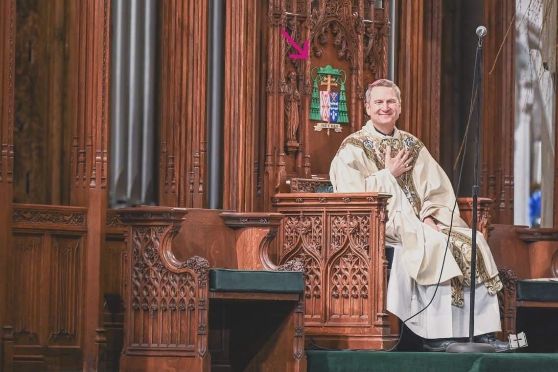 El escudo episcopal de muchos obispos tiene un lema en latín. El del arzobispo de Nueva York, Ronald Hicks, está en español y dice: PAZ Y BIEN, frase asociada al carisma franciscano.