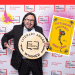 Smiling man in a suit holding a large circular 'Literary Award Winner' plaque with the Pen America logo; backdrop features 'The Freedom to Write'.
