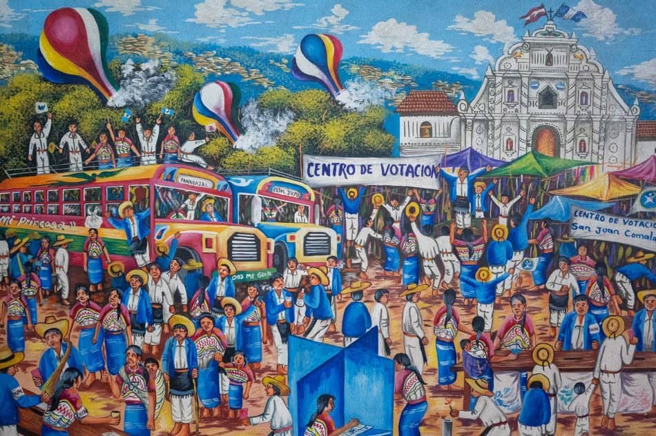Vibrant street scene of a voting center with banners, crowds in traditional blue-and-white attire, buses, and balloons.
