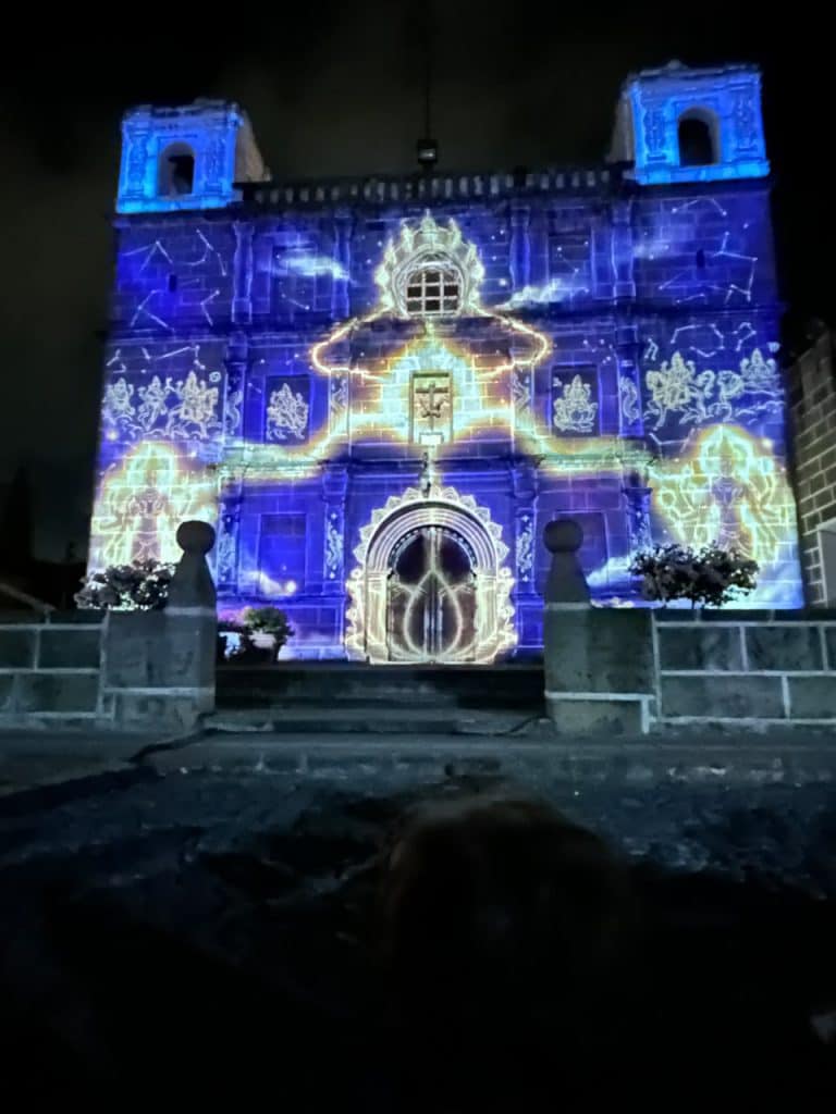Night view of a stone church façade illuminated by blue and gold projection art, highlighting arches and windows.