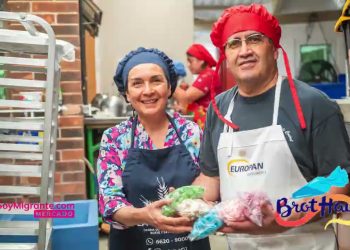 Smiling woman and man in aprons and hair nets hand out bags of vegetables in a busy community kitchen.