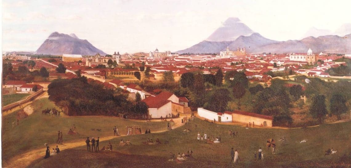 Panoramic view of a colonial town with red-roofed buildings and distant mountains; people picnicking on a grassy foreground.