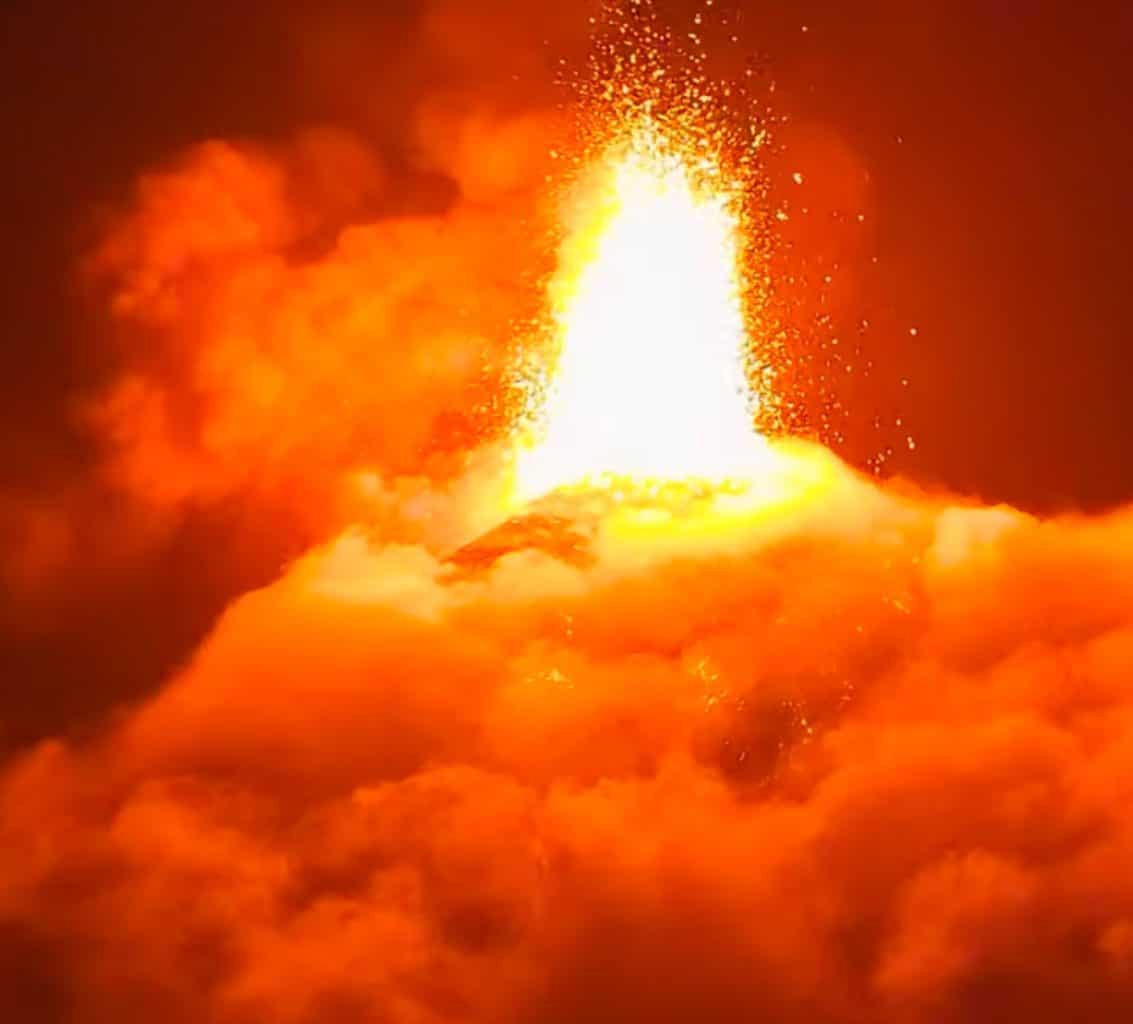 Intense lava fountain and orange plume erupting from a volcano at night with embers. Poignant volcanic eruption scene.