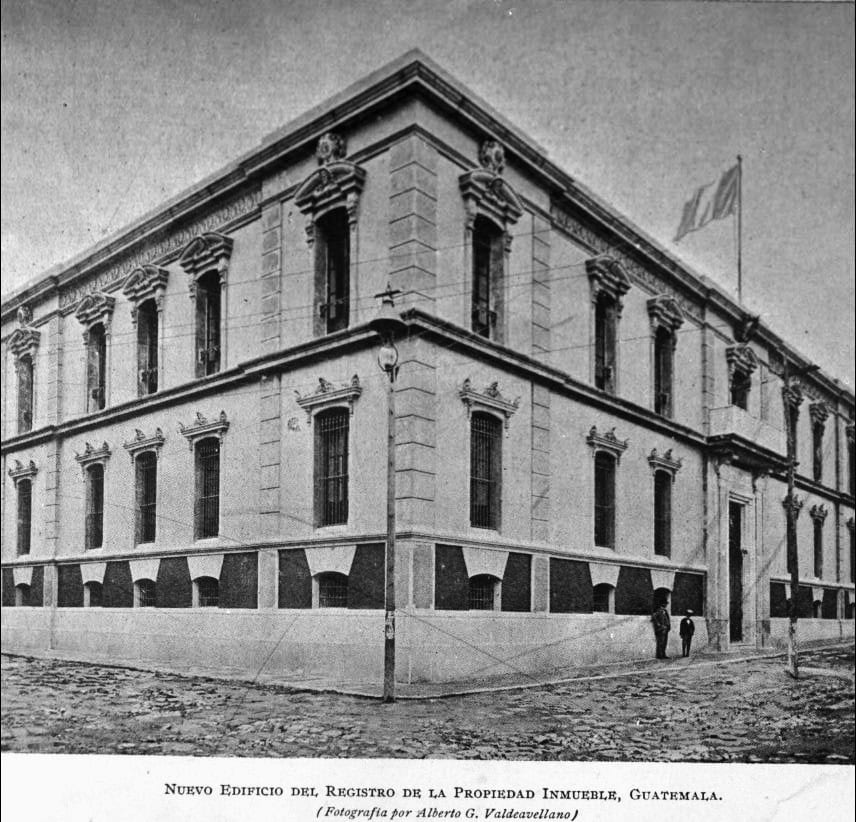 Nuevo Edificio del Registro de la Propiedad Inmueble, Guatemala: un edificio gubernamental histórico de dos pisos con ventanas decorativas y bandera en la azotea.