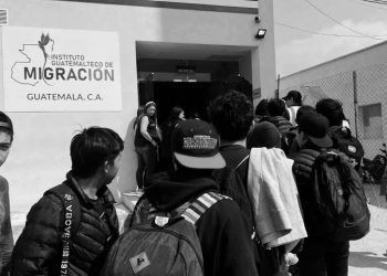 People with backpacks wait in a line outside the Centro de Recepción de Retornados at Guatemala's Instituto Guatemalteco de Migración.