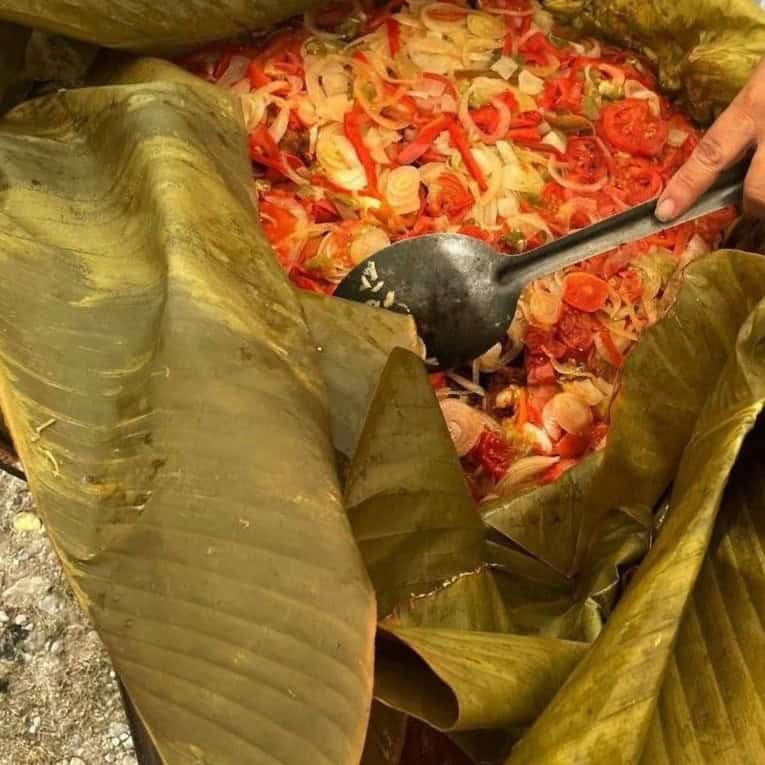 recetas guatemaltecas chal kuum o chalkun delicia mopan – SoyMigrante.com REVISTA Person scooping bright chopped vegetables (onions, peppers, tomatoes) from a large banana leaf–wrapped dish with a spoonble