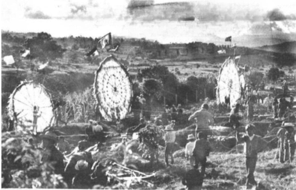 WWI battlefield scene with trenches, barbed wire, and soldiers advancing under a cloudy sky; flags in the distance.
