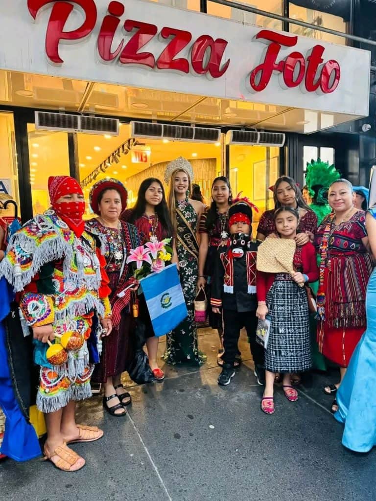 Group of people in colorful traditional attire posing outside a pizza shop.