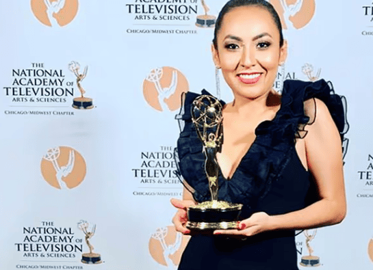 La guatemalteca Zully Ramírez ganó un premio Emmy de la televisión estadounidense en 2019, por su labor informativa – SoyMigrante.com REVISTA Smiling woman in a dark dress holds an Emmy statue at an awards event, with a branded backdrop.