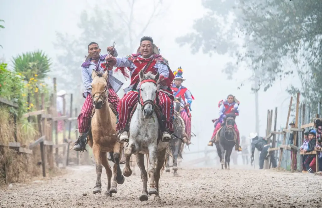 En la neblina comienzan a correr una y otra vez los todosanteros en memoria de los ancestros y celebrando la vida. La ebriedad es parte del juego y si alguien se cae, se levanta; si llega a fallecer por la caída, se considera una bendición. (Fotografía del festejo 2023 Abel Juarez, especial para SoyMigrante.com) – SoyMigrante.com – SoyMigrante.com