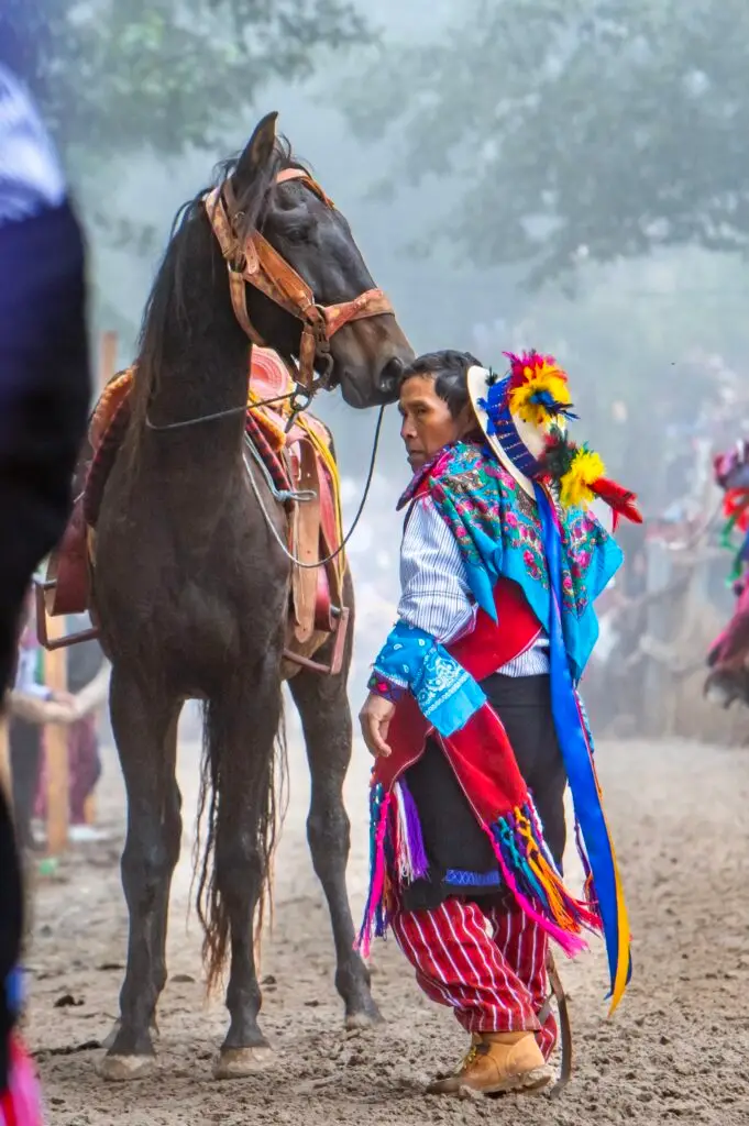 El atuendo tradicional de las carreras de Todos Santos Cuchumatán incluye sombrero decorado con plumas y pañuelos, para exhibir alegría y a la vez devoción por los espíritus de los ancestros. (Fotografía de la carrera 2023 por Abel Juárez, especial para SoyMigrante.com) – SoyMigrante.com – SoyMigrante.com