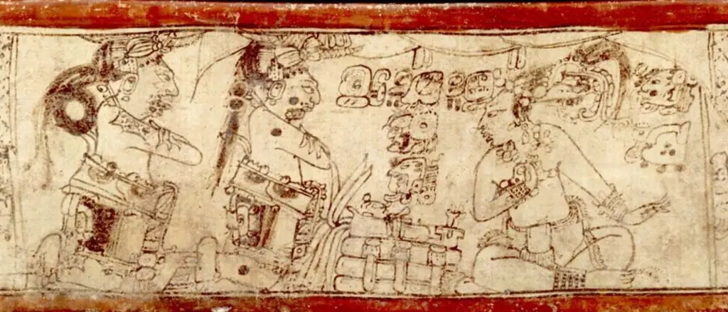 Los héroes mayas del Popol Vuh, Hunahpú e Ixbalanqué (gemelos, a la izquierda) conversan con un personaje identificado como el dios maya del Maíz, caracterizado por las largas hojas de su tocado, que aluden a la milpa. (Vaso hallado en Chamá, Alta Verapaz, fotografía de Justin Kerr) – SoyMigrante.com – SoyMigrante.com